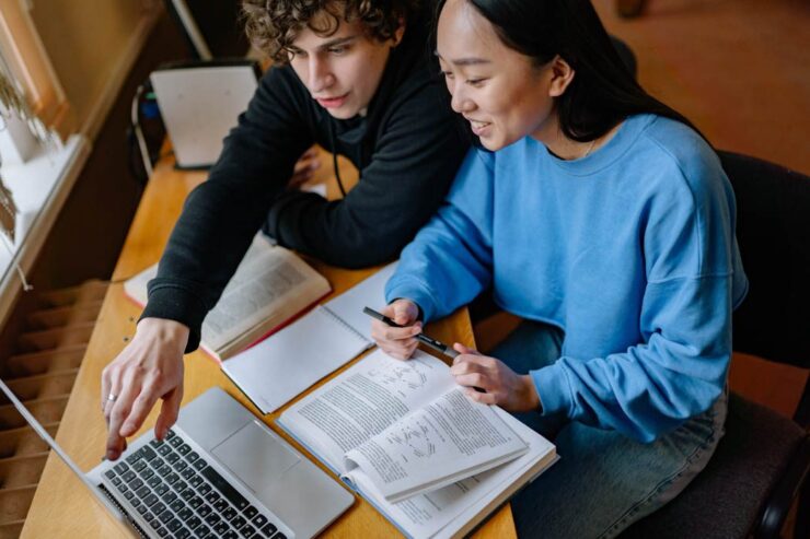 Two teachers reviewing a textbook and laptop.